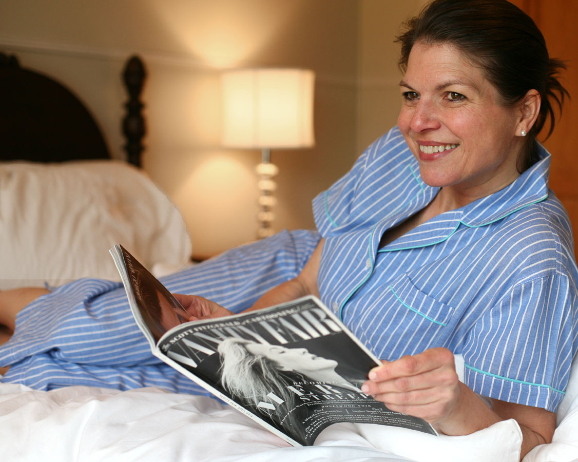 Woman reclining in pjs on a bed reading a magazine.
