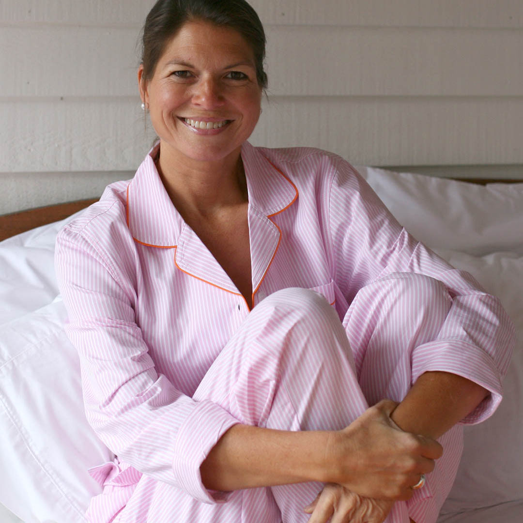 Woman sitting on a bed wearing long sleeve pink and white striped pjs.